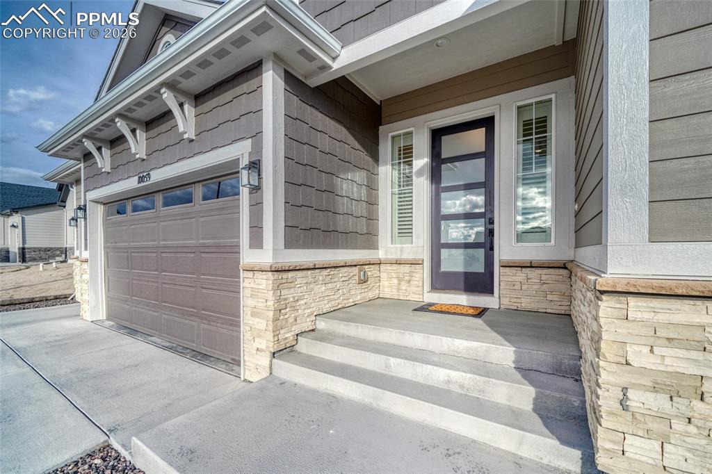 View of exterior entry with stone siding, covered porch, driveway, and an attached garage