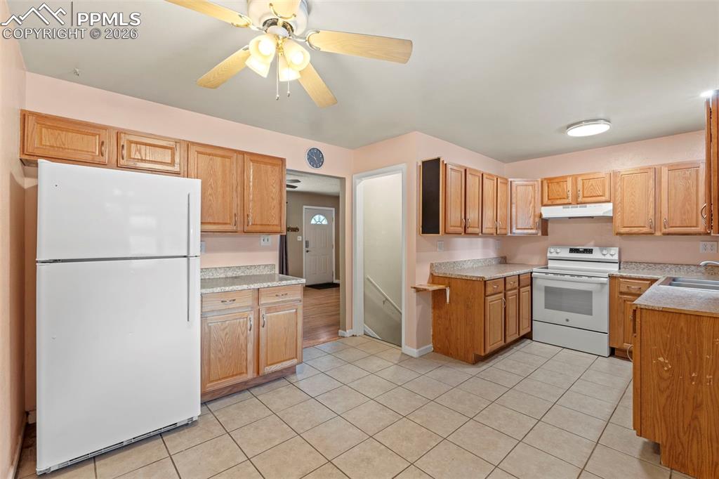Kitchen featuring white appliances, light countertops, a ceiling fan, under cabinet range hood, and light tile patterned floors