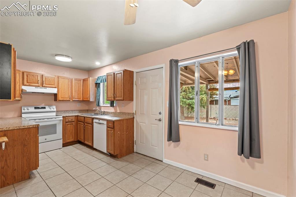 Kitchen featuring white appliances, plenty of natural light, light tile patterned floors, and under cabinet range hood