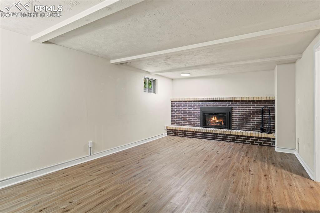 Unfurnished living room with a textured ceiling, a fireplace, light wood-type flooring, and beam ceiling