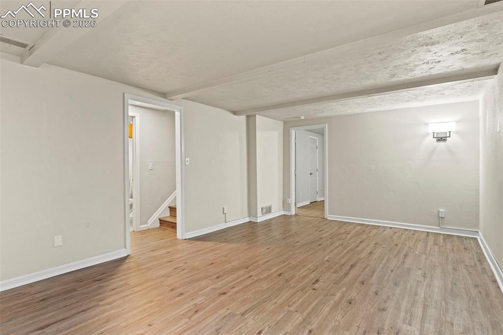 Empty room featuring beamed ceiling, light wood-style flooring, stairs, and a textured ceiling