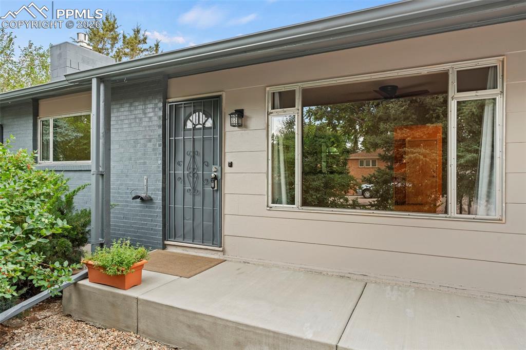 View of exterior entry with brick siding, a chimney, and covered porch