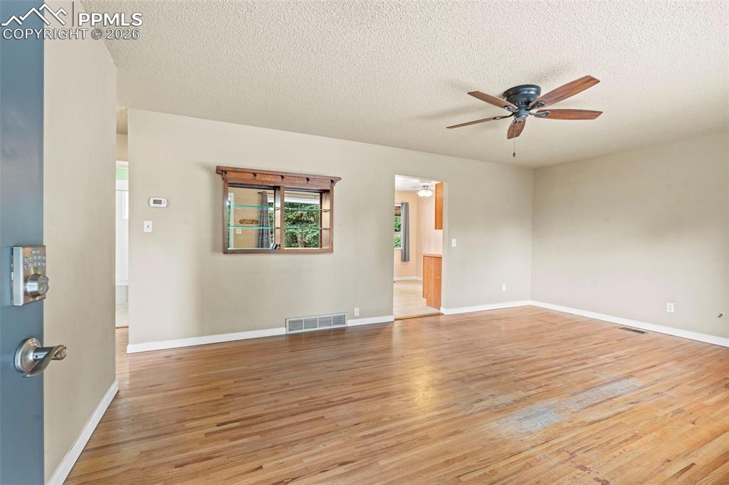 Empty room with light wood-style floors, a textured ceiling, and a ceiling fan