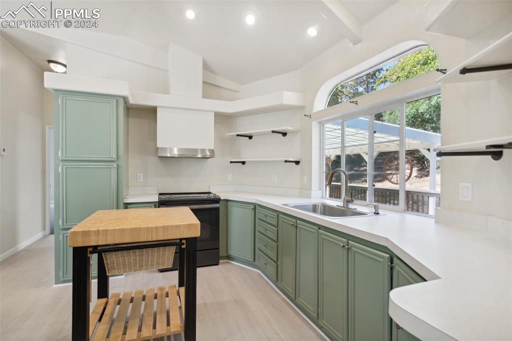 Kitchen with black range, light hardwood / wood-style floors, green cabinets, and sink