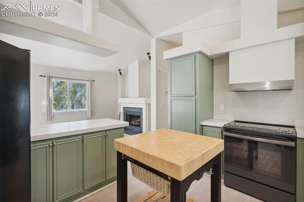 Kitchen with vaulted ceiling, black refrigerator, light hardwood / wood-style flooring, stainless steel range with electric cooktop, and green cabinets