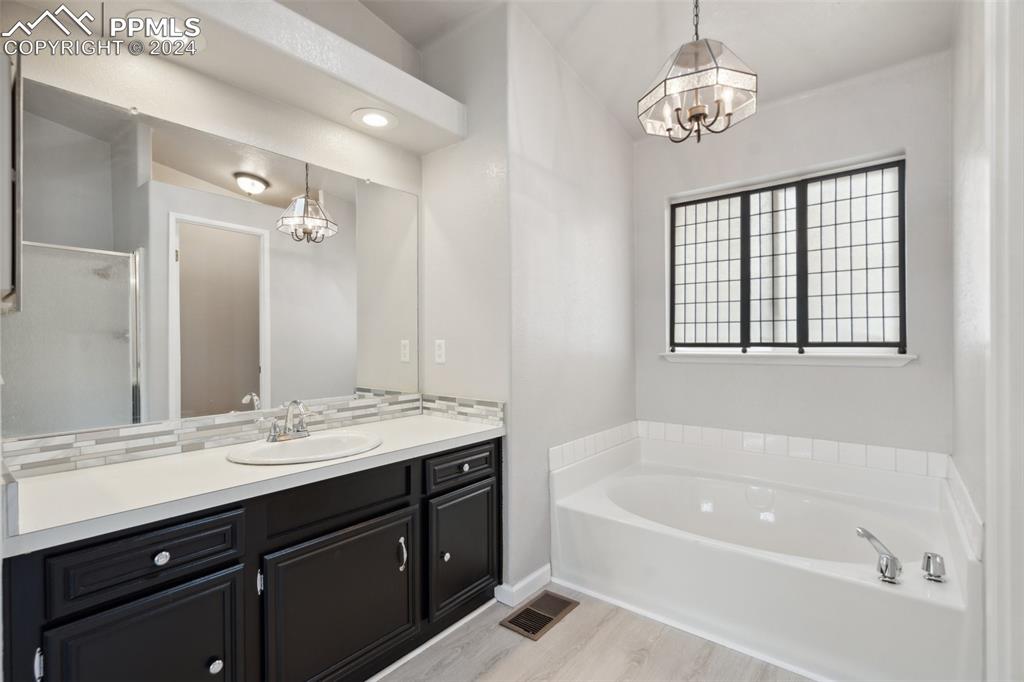 Bathroom with vanity, separate shower and tub, a chandelier, and hardwood / wood-style flooring