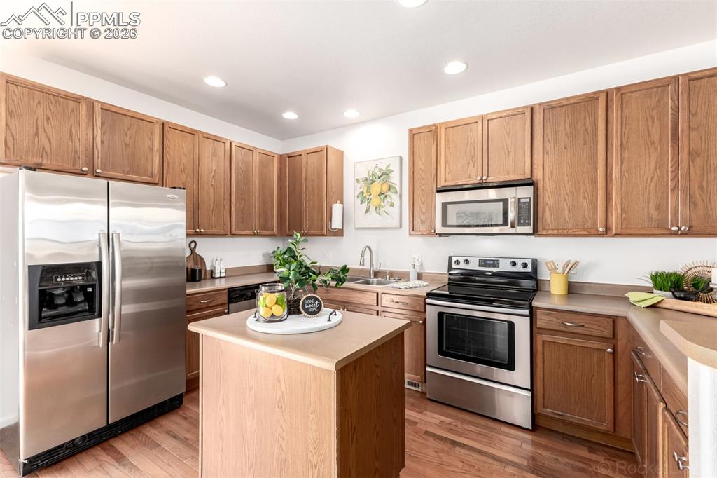Stainless steel appliances, light countertops, light wood-style flooring and a center island