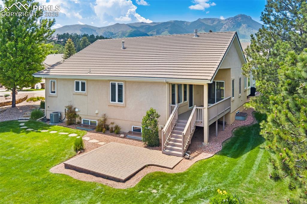 Back of property with a mountain view, central AC, a patio, a yard, and stucco siding