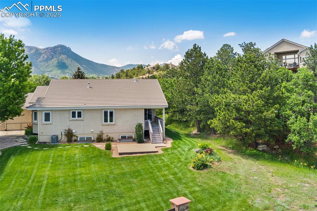 Rear view of property featuring stucco siding, a lawn, a mountain view, cooling unit, and stairs