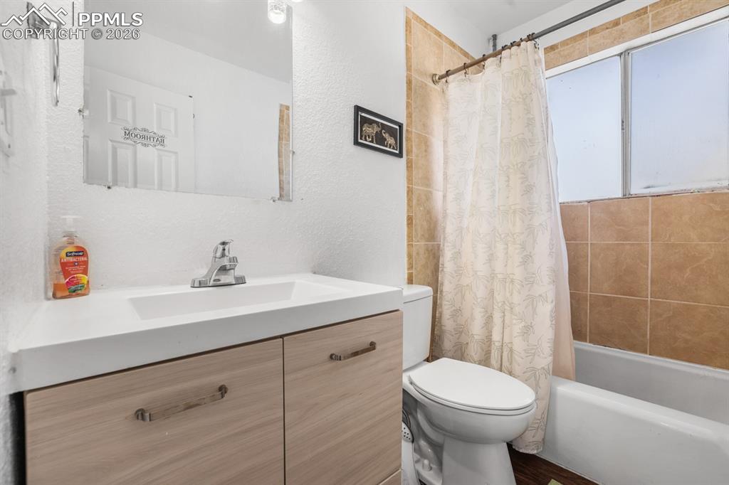 Bathroom with vanity, shower / bath combination with curtain, and a textured wall