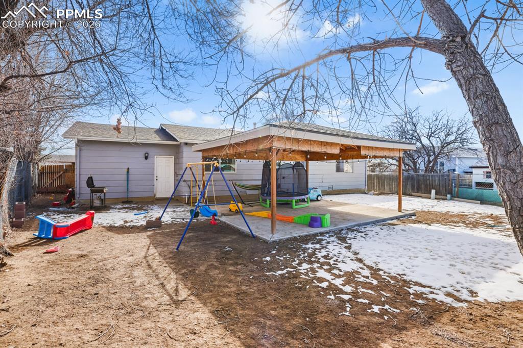 Rear view of property featuring a playground, a fenced backyard, a patio area, and roof with shingles