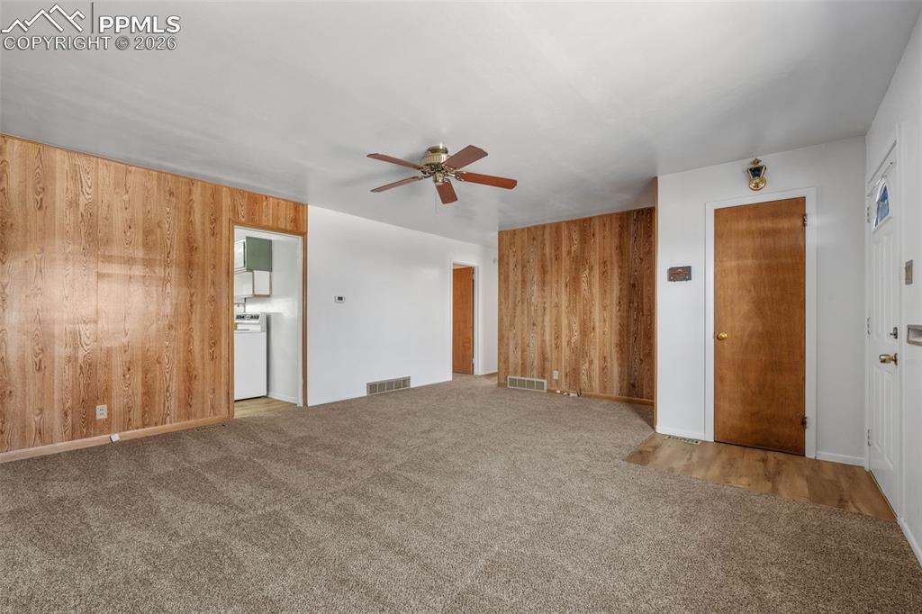 Unfurnished living room with wood walls, light carpet, and ceiling fan