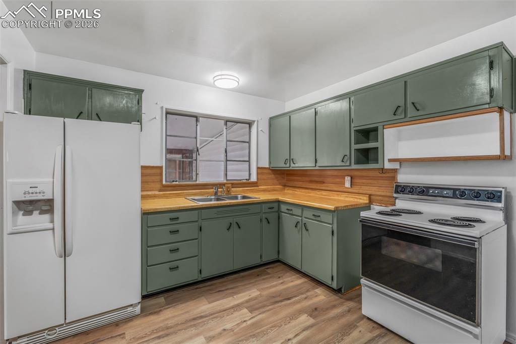 Kitchen featuring green cabinets, white appliances, light countertops, light wood-style floors, and open shelves