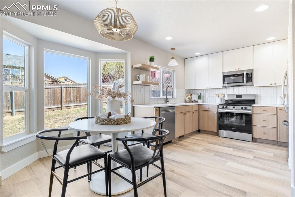 Two tone kitchen with light countertops, stainless steel appliances, backsplash, two tone cabinets, and open shelves