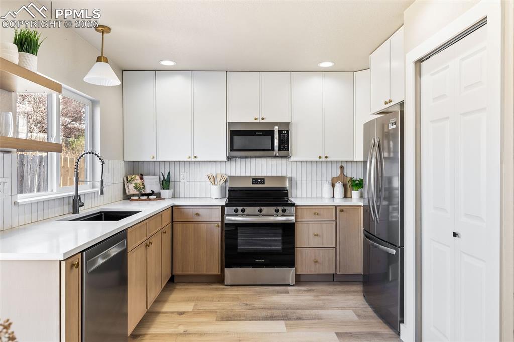 Two tone kitchen featuring dual tone cabinetry, stainless steel appliances, decorative light fixtures, light wood-type flooring, and light stone countertops