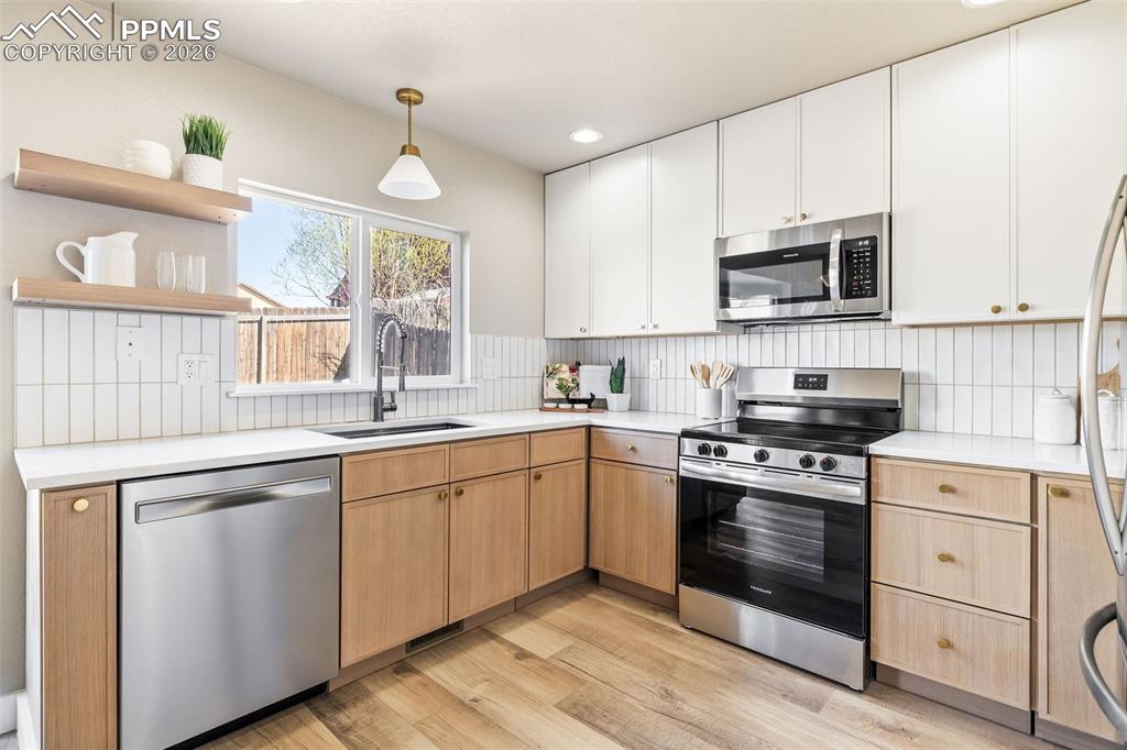 Two tone kitchen featuring stainless steel appliances, open shelves, two tone cabinetry, light wood-style flooring, and decorative light fixtures
