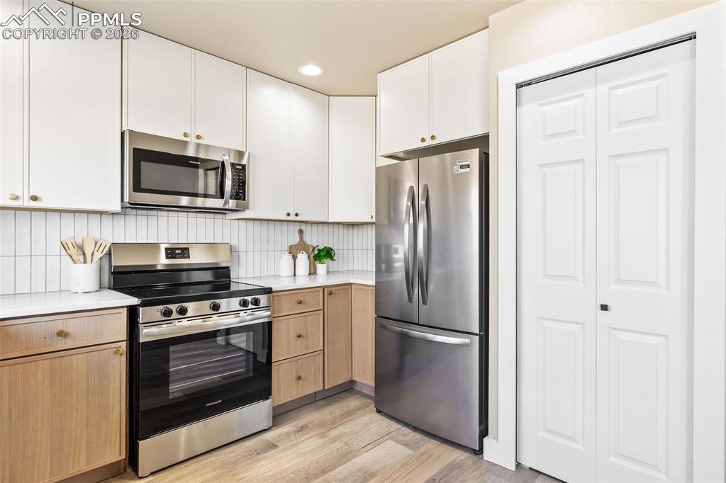 Two tone kitchen featuring stainless steel appliances, light wood-style flooring, two tone color scheme, recessed lighting, and tasteful backsplash