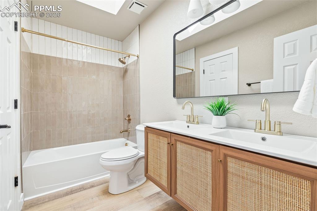 Bathroom with double vanity, washtub / shower combination, and light wood-style flooring