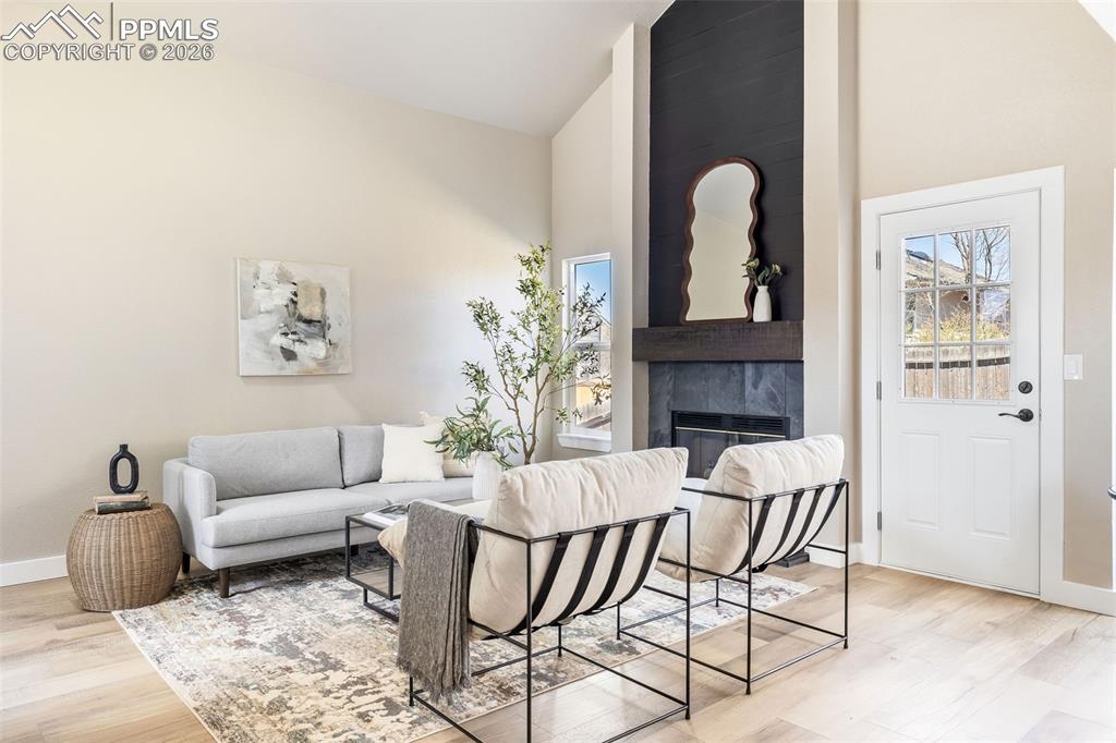 Living room with vaulted ceiling, light wood-style floors, and a high end fireplace