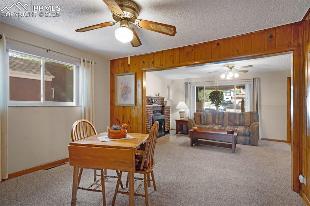 Dining space with light colored carpet, wood walls, a fireplace, and a textured ceiling