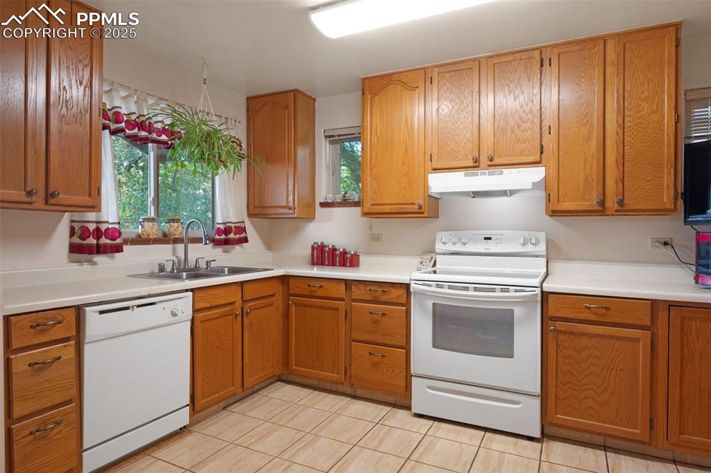 Kitchen featuring white appliances, brown cabinets, light countertops, under cabinet range hood, and light tile patterned flooring