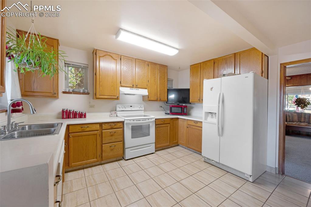 Kitchen with light countertops, white appliances, light tile patterned flooring, and under cabinet range hood