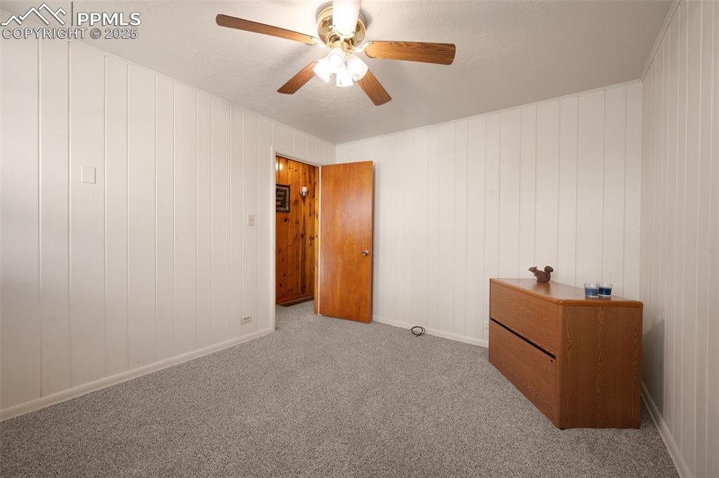 Unfurnished bedroom featuring carpet flooring, ceiling fan, and wood walls