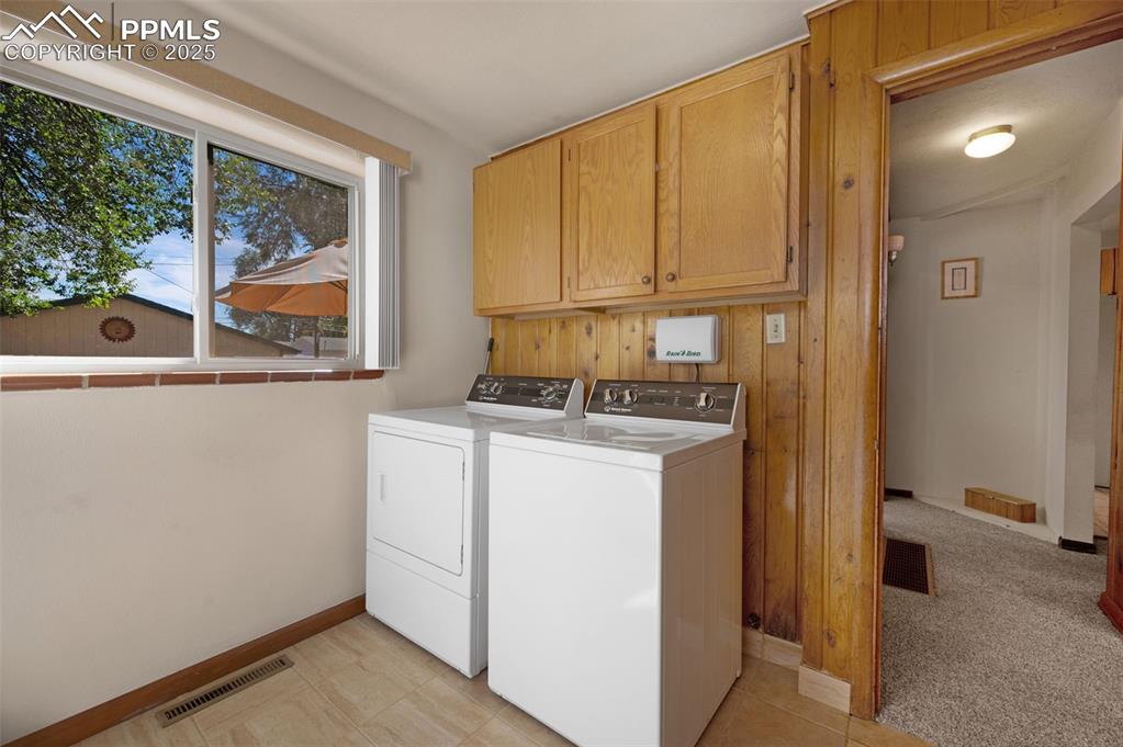Washroom featuring cabinet space, washing machine and dryer, light colored carpet, and wooden walls