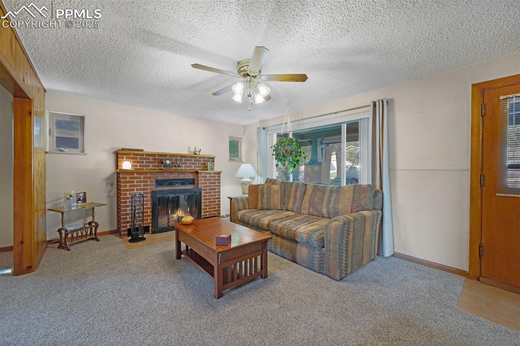 Carpeted living room featuring a fireplace, a textured ceiling, and ceiling fan