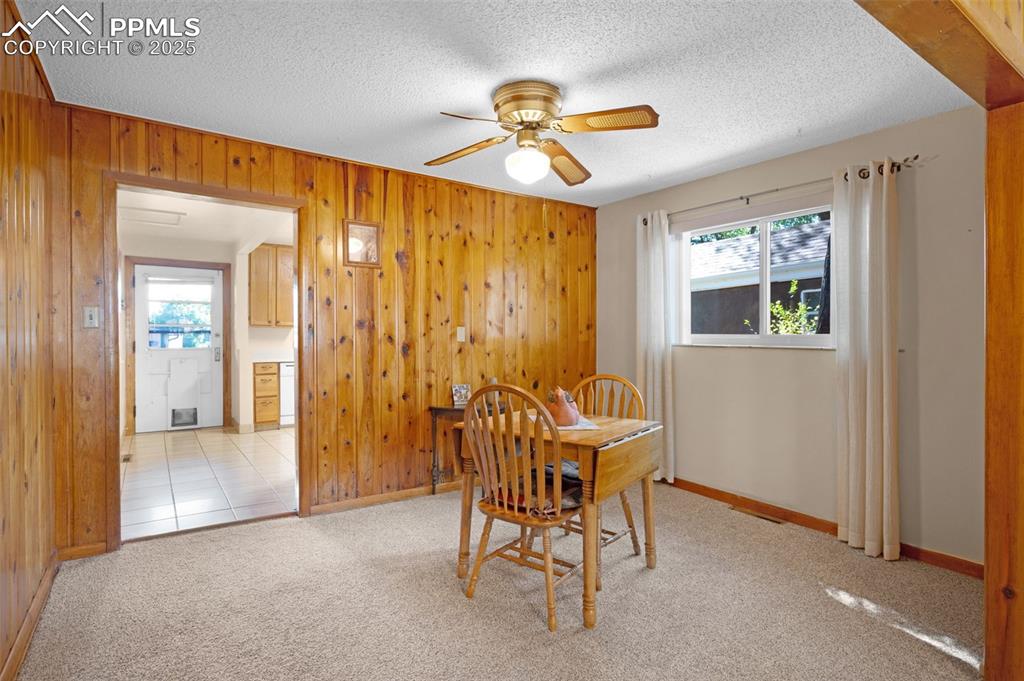 Carpeted dining area with wood walls, a ceiling fan, and a textured ceiling