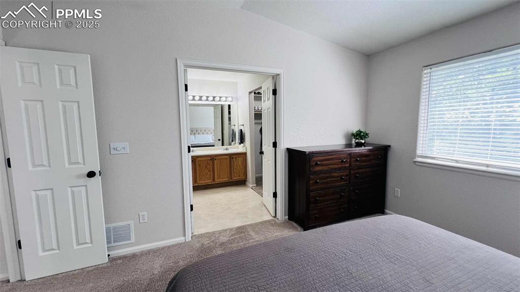 Bedroom featuring a textured wall, light colored carpet, connected bathroom, and vaulted ceiling