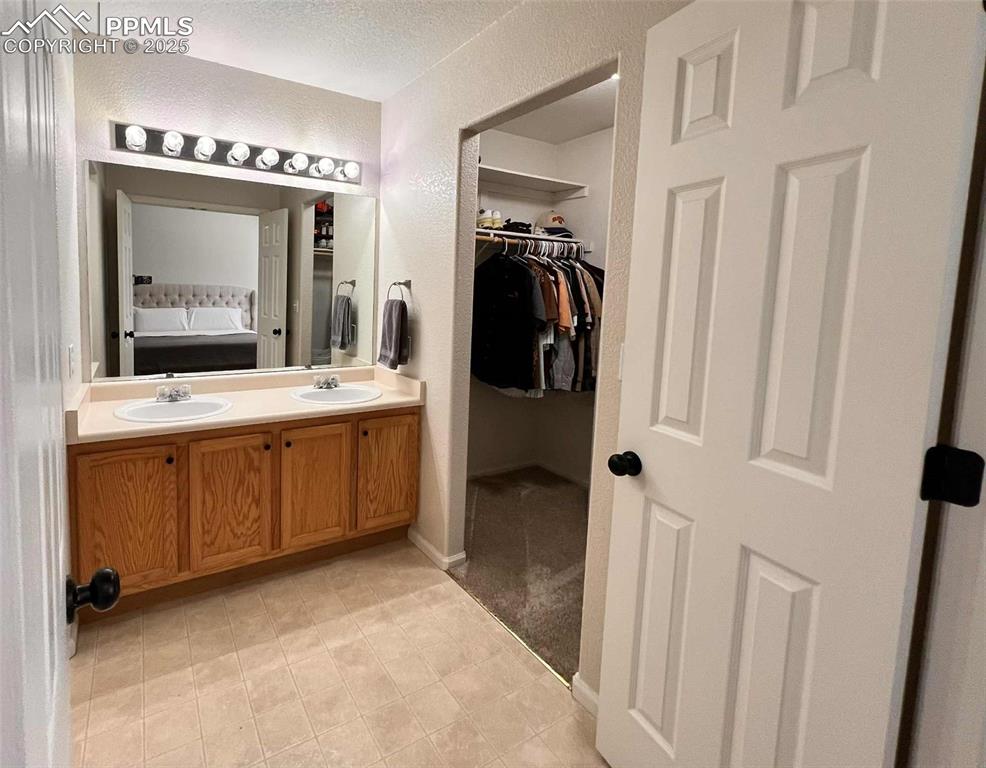 Bathroom featuring a spacious closet, double vanity, a textured wall, and a textured ceiling