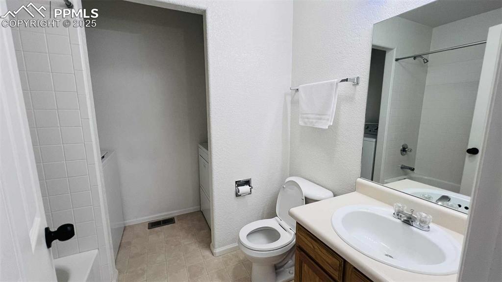 Bathroom with vanity, a textured wall, shower / bath combination, and washer / clothes dryer