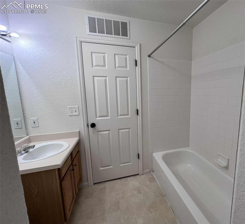 Full bath featuring vanity, a textured wall, tile patterned floors, and shower / bath combination