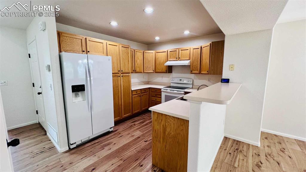 Kitchen with white appliances, a peninsula, recessed lighting, light wood finished floors, and light countertops