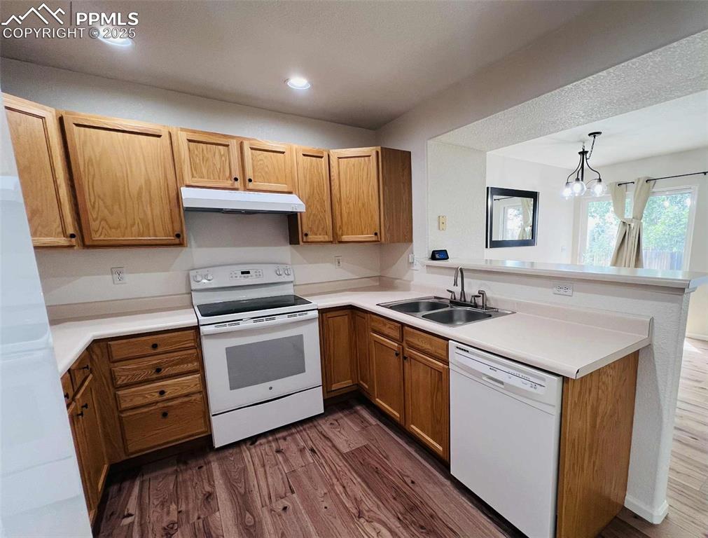 Kitchen with white appliances, a peninsula, dark wood finished floors, under cabinet range hood, and light countertops