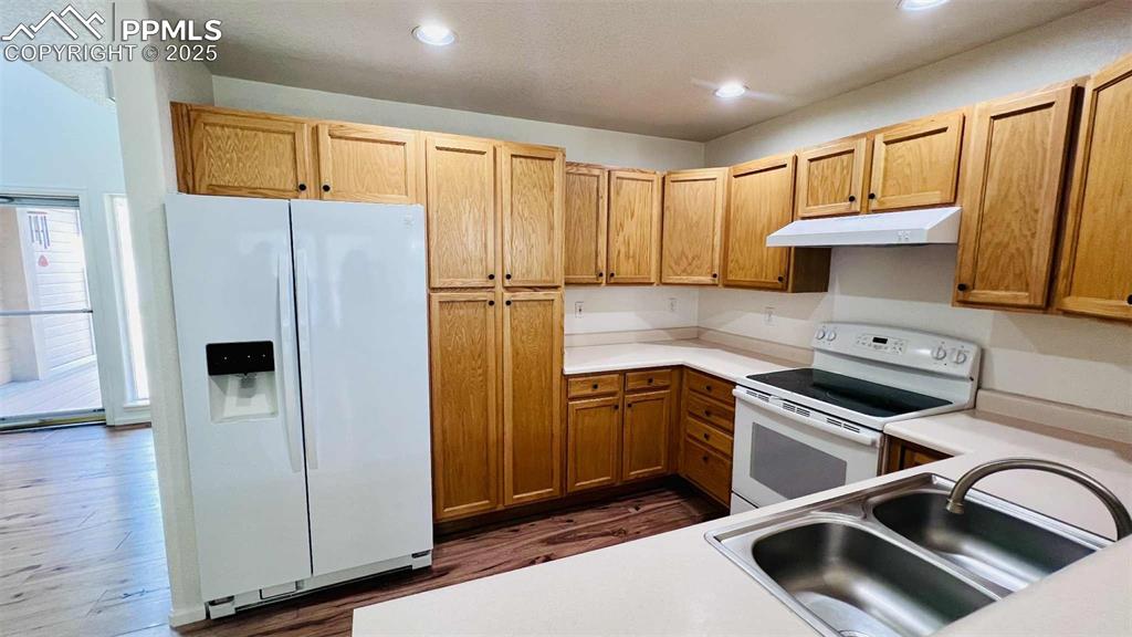 Kitchen featuring white appliances, under cabinet range hood, light countertops, dark wood-style flooring, and recessed lighting