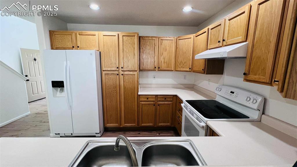 Kitchen with white appliances, light countertops, under cabinet range hood, wood finished floors, and recessed lighting