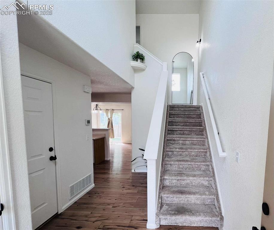 Stairway featuring wood finished floors, a textured wall, and a towering ceiling