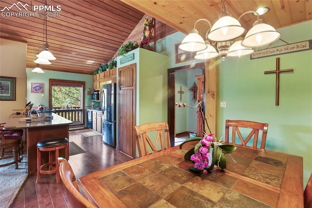 The dining room with wood ceiling, dark wood-style flooring, and lofted ceiling wooden trim overlooking the kitchen!