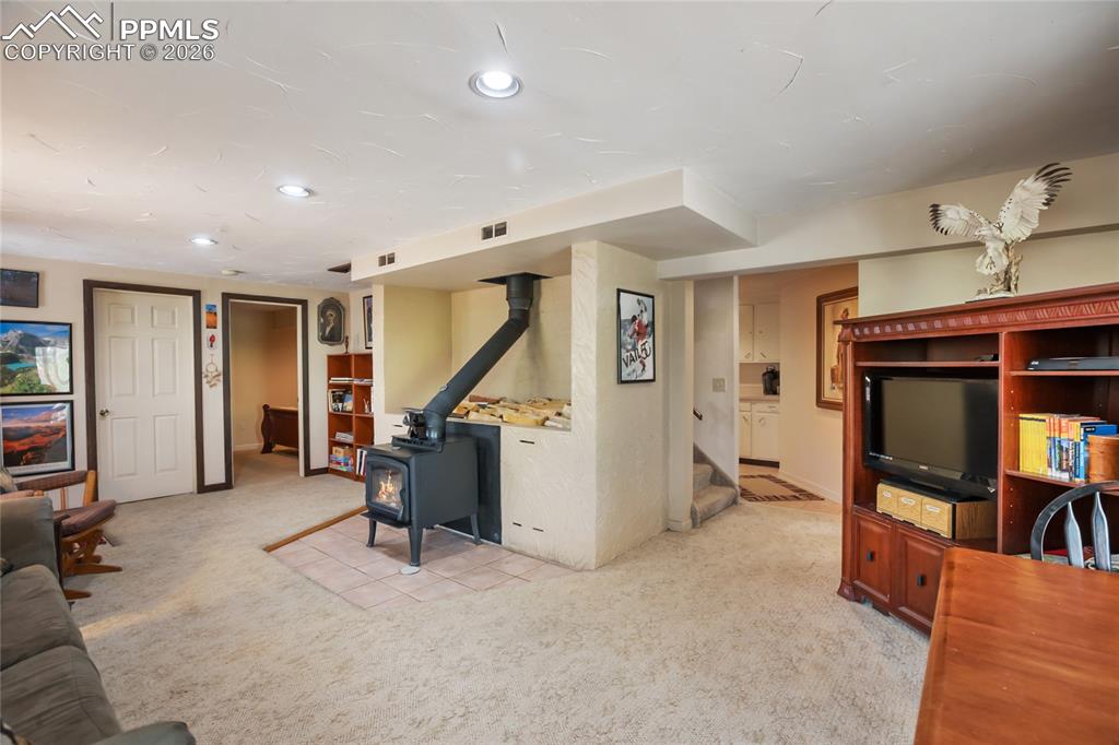 The downstairs family room with a wood stove, light carpet, stairs, and recessed can lighting!