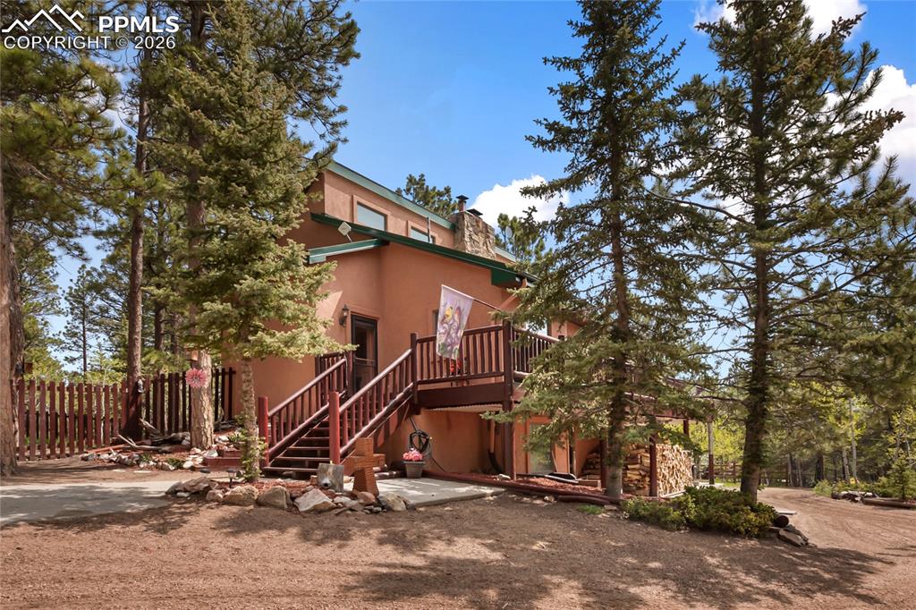 Side of the home with stucco siding, stairs, a wooden deck, and a rock chimney with lots of mature trees!