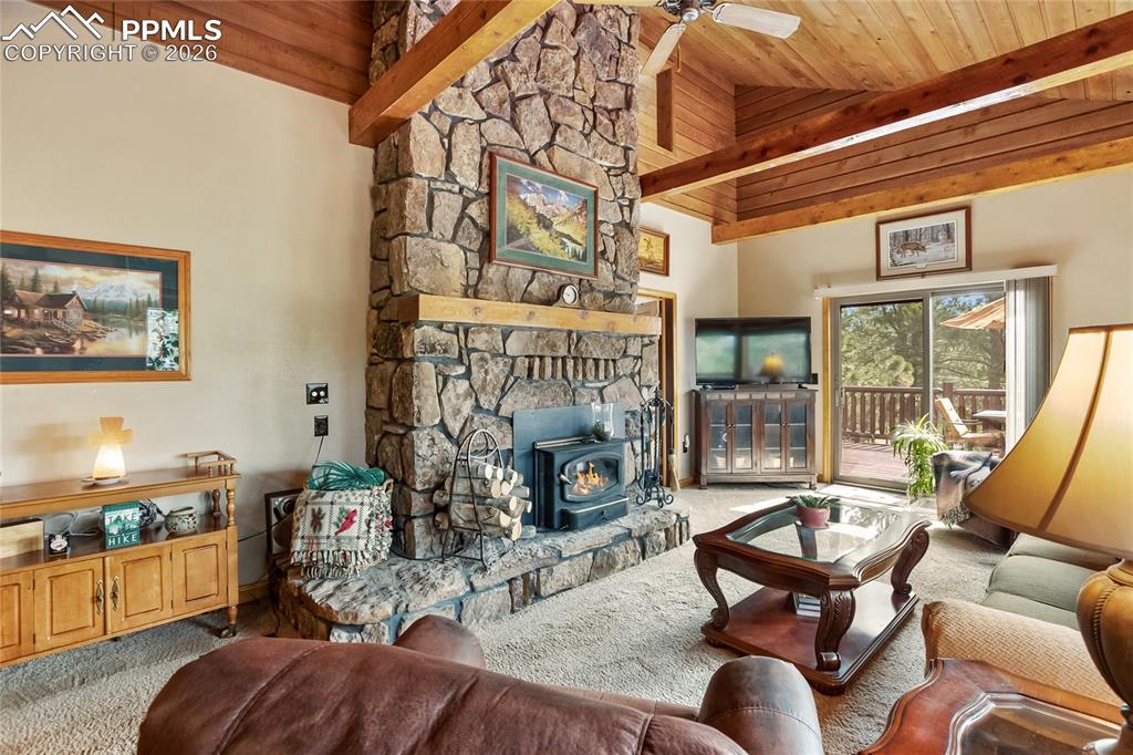 The cozy living room has a high vaulted wood ceiling with exposed beams, a ceiling fan, and a cozy wood stove!