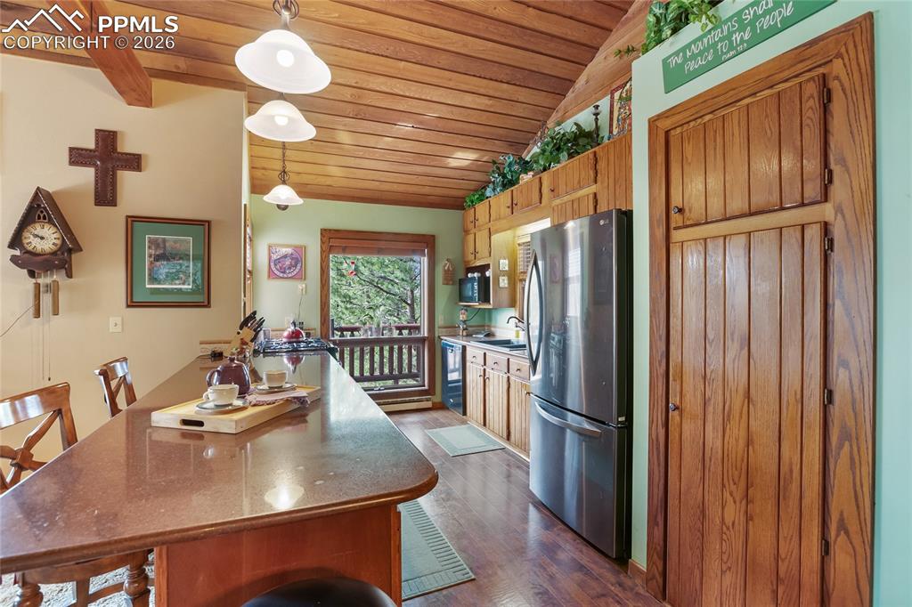 Kitchen with a kitchen bar, wooden lofted ceiling, freestanding refrigerator, and decorative light fixtures!