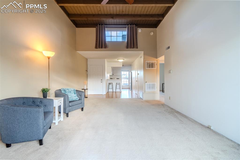 Sitting room featuring a high ceiling, a wood ceiling with exposed beams, and carpet