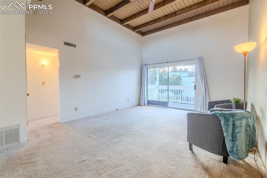 Living room featuring a towering ceiling, carpet floors, and a wood ceiling with exposed beams