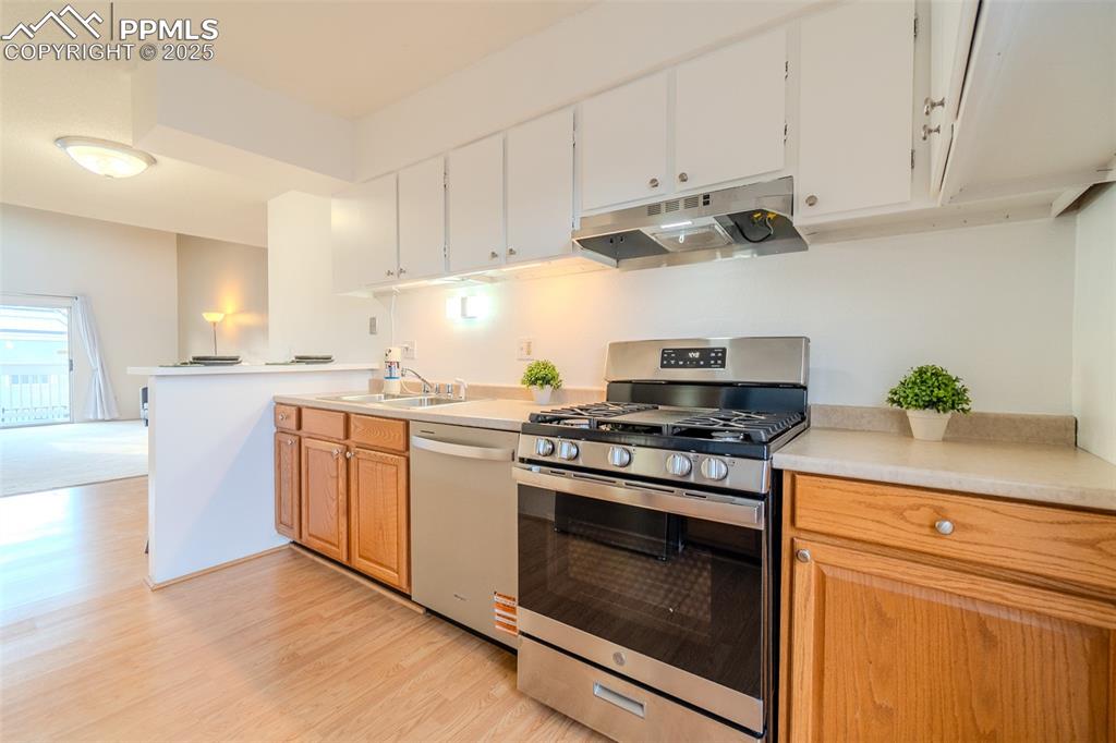 Kitchen with stainless steel appliances, light countertops, under cabinet range hood, light wood-style floors, and white cabinetry