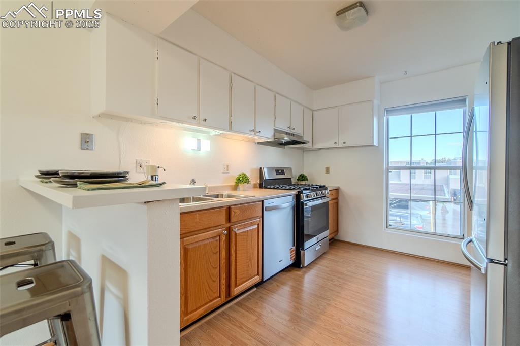 Kitchen with stainless steel appliances, light countertops, light wood-style floors, white cabinets, and under cabinet range hood