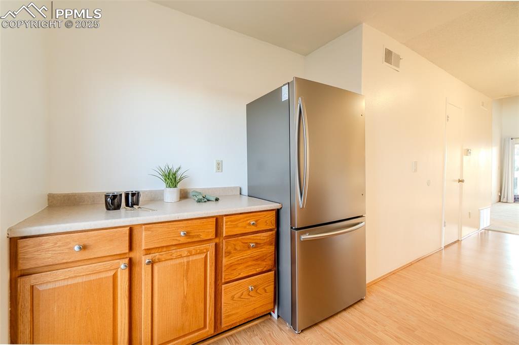 Kitchen with freestanding refrigerator, brown cabinetry, light wood-style floors, and light countertops