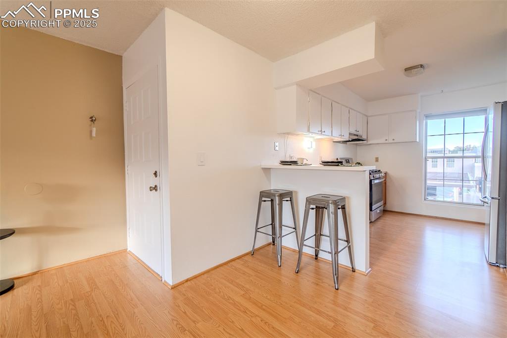 Kitchen featuring a breakfast bar area, white cabinetry, light wood-type flooring, appliances with stainless steel finishes, and light countertops